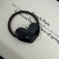 Detail of a handmade black heart-shaped hair tie with golden logo on beige fabric - Black