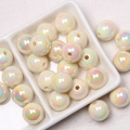 Macro shot of 16mm beige acrylic iridescent beads with center holes on ceramic plate - Cream