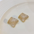 Golden square earrings with beige marble enamel finish displayed on a white plate - Milky Apricot