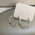 Dettaglio di orecchini a cerchio argento con texture geometrica su cartoncino - Argento