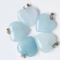 Polished light blue crystal heart pendants with silver metal clasps on white background - Synthetic Aquamarine
