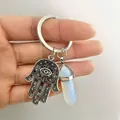 Close-up of silver Hamsa Hand pendant with a white hexagonal crystal on the keychain - Opal
