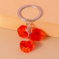 Detailed view of three translucent orange-red heart pendants on a silver keychain - Red