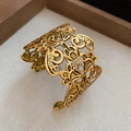 Detailed close-up of a vintage hollow-out gold flower cuff bracelet on beige fabric - Gold