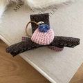 Close-up of a tweed hair claw clip featuring a knitted bag charm on a book background - Hair Claw-Pink-Bag