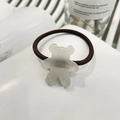 Detail view of transparent bear charm with text on a brown elastic hair tie - Bear Cookie Hair Tie / White