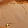 Detail of a gold pumpkin ghost pendant on a fine necklace chain against silk fabric - Pumpkin Necklace (Gold)