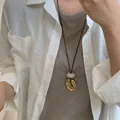 Detail van een ronde acryl kraal en matte gouden ring aan een lang zwart koord sieraad - 1# Gouden Onregelmatige Ring Met Crèmewitte Kraal (HN7339)