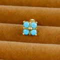Vue macro d'un piercing croix doré avec pierres turquoise sur plateau en velours - Croix / Or / Bleu Ciel
