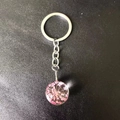 Macro shot of silver keychain featuring a glass bulb with preserved pink dried flowers - Pink Lace Flower