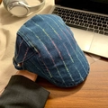 Detail of blue denim beret with colorful stitching and adjustable strap on a desk - Mid Blue Rainbow Stripe