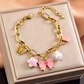 Bracciale dorato con ciondoli in smalto rosa, fiocchi e perle su una scatola da gioielli - Bracciale