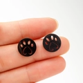 Macro shot of black cat paw earrings with heart cutout held between fingers - Black