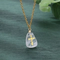 Detail view of a gold water-drop stone pendant with an inner cross on green wood background - White