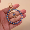Detaillierte Nahaufnahme des goldenen Hamsa-Schlüsselanhängers mit blauen Augen-Perlen - Kleine Augenpalme