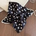 Details des schwarzen Scrunchies mit Blumenmuster und weißen Perlen am Rand auf Holz - Scrunchie / Schwarz Blumig Mit Perle