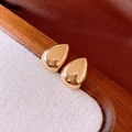 Detailed close-up of polished gold teardrop earrings on a white textured display board - Gold