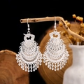 Detailed shot of ethnic silver hollow peacock earrings hanging on a rustic wooden branch - 4-Layer Silver Phoenix