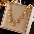 Minimalistische goldene Titanstahlkette mit Kugelanhängern auf einer beigen Schmuckschatulle - Gold