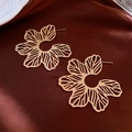 Close-up of golden hollow flower earrings on luxurious dark red satin background - Gold