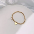 Close-up of golden beaded stretch bracelet with pearl charm and heart tag on white silk - Gold Heart