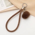 Détail d'un porte-clés en tissu tressé marron avec pompon en peluche et crochet en argent - café