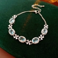 Macro shot of silver bracelet with blue oval stones and white zircon flowers on green velvet - Blue
