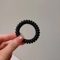 Dettaglio dell'elastico a spirale nero opaco tenuto in mano su sfondo beige neutro - Nero