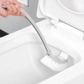 Grey bathroom toilet brush with white bristles cleaning the rim of a white toilet bowl - Gray
