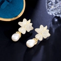 Dettaglio di orecchini a fiore dorati con zirconi e perle a goccia su sfondo nero lucido - Oro