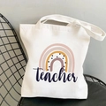 Detail view of white canvas tote bag with rainbow print and teacher text on a chair - Dark Blue Text Teacher