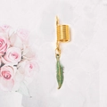Detalle de anillos dorados para rastas con colgantes de plumas de bronce sobre flores - Estilo de Hoja