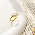 Detailaufnahme eines tropfenförmigen Zirkonia-Goldrings an Keramik mit Vintage-Buch - US 7 / Gold - Gebogener Tropfen Zirkon