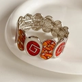 Detalle macro de pulsera elástica vintage con logo G de esmalte rojo y estrellas naranjas - Plata-Amarillo-Rojo