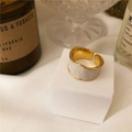 Primer plano de anillo ondulado dorado con esmalte blanco sobre un pedestal blanco - Blanco