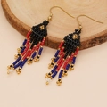 Detail view of Bohemian seed bead tassel earrings on a natural wood surface - Black Red Blue Gold