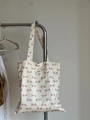 Detail of off-white canvas tote bag featuring pink bow patterns and shoulder strap hanging - Light Blue Polka Dot Pink Bow