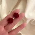 Élégantes boucles d'oreilles rose en velours rouge présentées à la main en gros plan - Rose Floconnée Rouge (0009)