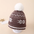 Close-up of brown knitted winter hat featuring white snowflakes and a fluffy pom-pom top - Approx. 3-10 years old / Brown