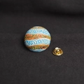 Round ceramic badge with blue, orange, and green wave pattern and golden butterfly clutch - Jupiter Style