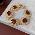 Dettaglio di un bracciale vintage dorato con pietre ovali marroni e accenti floreali - Bracciale Rosso