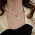 Gros plan d'un pendentif cœur en perle sur un collier doré porté par un mannequin - Collier avec pendentif coeur en perles blanches