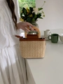 Detail of hand-woven straw bucket bag with dark brown leather trim and wooden handles - Brown