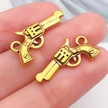Pendentifs revolvers dorés en métal pour bijoux DIY présentés sur le bout des doigts - Pistolet Revolver (19252) / 11x21mm