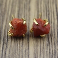 Macro shot of irregular orange raw mineral stones set in golden four-prong earrings - Sunstone