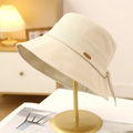 Detail of a chic beige cotton bucket hat with a bow and small metal tag on a stand - Beige