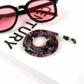 Close-up of Bohemian style braided eyewear strap coiled on a white book with sunglasses - US 11