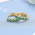 Elegante goldene Creolen mit grünen Zirkoniasteinen auf strukturiertem blauem Hintergrund - Kupfer / Gold Grün Zirkonia