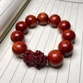 Close-up of red sandalwood beads bracelet with carved PiXiu charm on calligraphy book - High Density Blood Sandalwood Pi Xiu Lucky Style 20mm