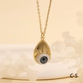 Close-up of golden Evil Eye pendant on warm beige background with white petals - Light Blue Drop-C5